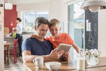 A father and son using a tablet while having breakfast