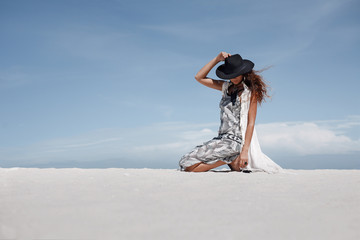 attractive boho girl siiting on sand at blue sky background