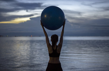 Silhouette yoga ball yong woman in the beach sunset background.