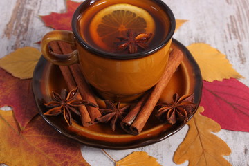 Cup of tea with lemon, spices and autumnal leaves on wooden background