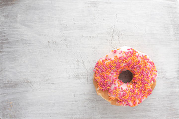 frosted donut with pink sprinkles on a weathered wood background. Isolated, copy space