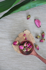 Spoon of Dried Roses on Background with Green Leaves