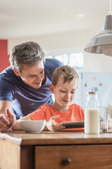 A father and son using a tablet while having breakfast
