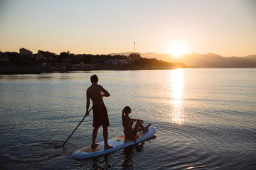 Silhouette of man and young sexy girl sitting on sup surf . Concept lifestyle, sport, love