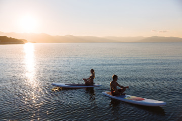 Silhouette of male and female in yoga pose on sup surf swimming at the ocean. Concept lifestyle, sport, love