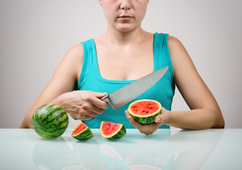 Girl using big knife for cutting juicy red small watermelons