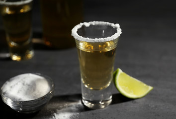 Gold tequila shot with lime and salt on gray background