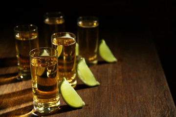 Gold tequila shots with lime on wooden table