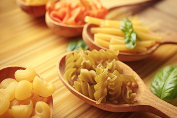 Different dry pasta on wooden spoons, close up