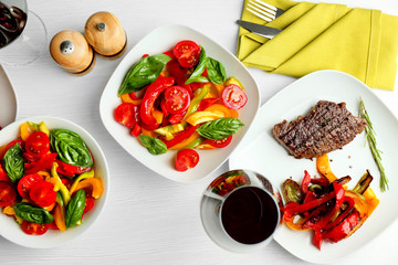 Tasty steak with vegetable salad and glass of wine on table