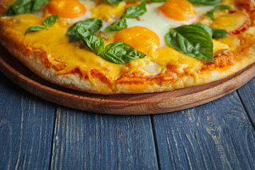Margarita pizza with basil leaves and egg on wooden table closeup