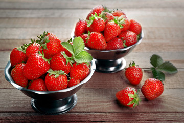 Metal bowls with fresh strawberries on wooden background