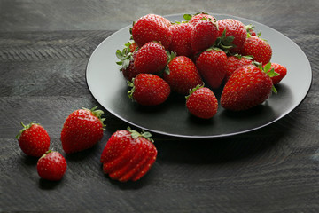 Black plate with ripe strawberries on dark wooden background