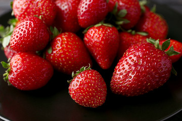 Black plate with ripe strawberries, closeup