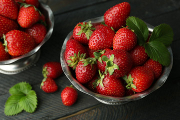 Metal bowls with ripe strawberries on dark wooden background