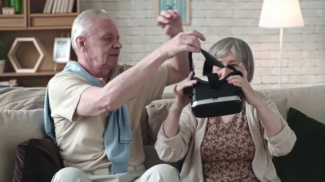 Medium shot of elderly man putting virtual reality goggles on senior woman for her to try them