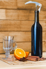 Ingredients for mulled wine: a bottle of , glass, orange cinnamon star anise Thatched sugar on  stand   background  brown wood