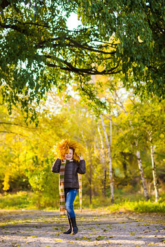 a teenager girl in jacket and jeans plays in the autumn park with golden leaves