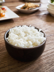 Cooked jasmine rice in a bowl on wooden table with food background