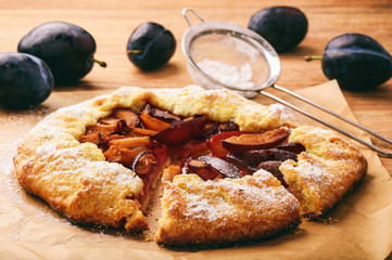 Rustic plum pie on brown wooden background.