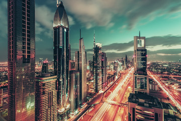 Obraz premium Bright colorful urban landscape of a big modern city with illuminated skyscrapers. Aerial view over downtown Dubai, UAE, with the famous highway. Artistic travel and architectural background.