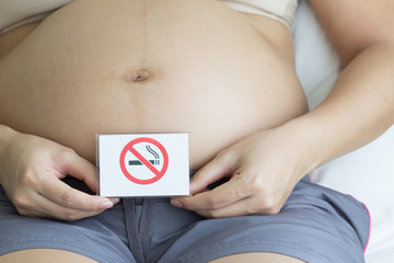 Pregnant woman holding lable with smokeing ban in bedroom.
