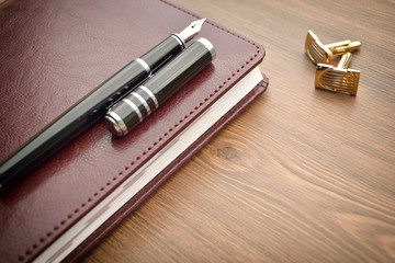 Business accessories on desktop: notebook, diary, fountain pen, cufflinks. 