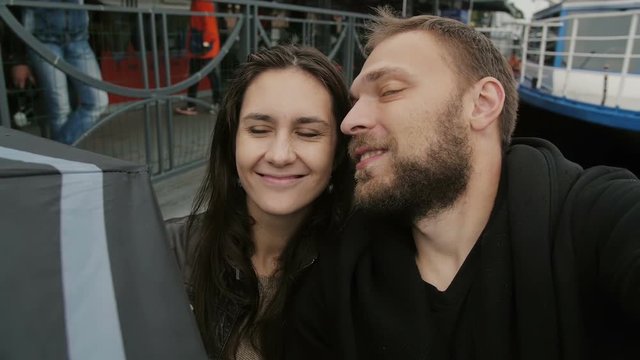 Happy couple taking selfie, point-of-view shot. man and a woman in love smiling at camera, kissing on a cheek, slow mo