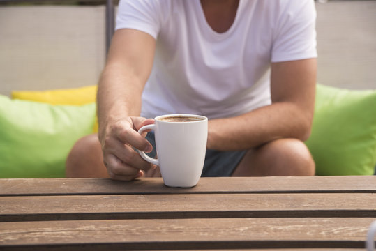 Mature man holding a cup of coffee on wooden table in green summ
