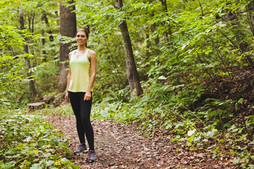 Woman runner standing on path in green forest during training