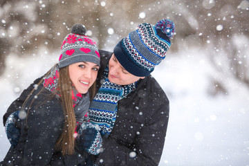 Loving couple embracing in winter park. They put colored caps and scarves. Loving warm hands to each other. Copy space. The girl hat with red hearts, snowfall