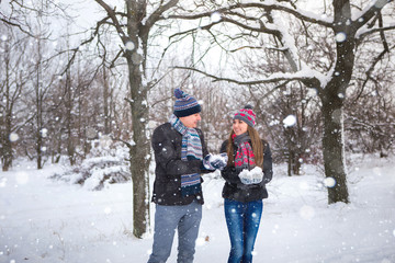Fototapeta na wymiar Couple in the park in winter throws snow up. People dressed in colorful hats and scarves romantic. Snowfall, copy space. Couple smiling, happy. Stroll in the park. The girl hat with hearts.