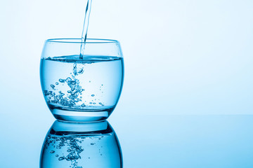 Pouring water into glass on blue background