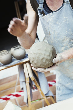 A potter handling a ball of wet clay pot, moulding and working it. 