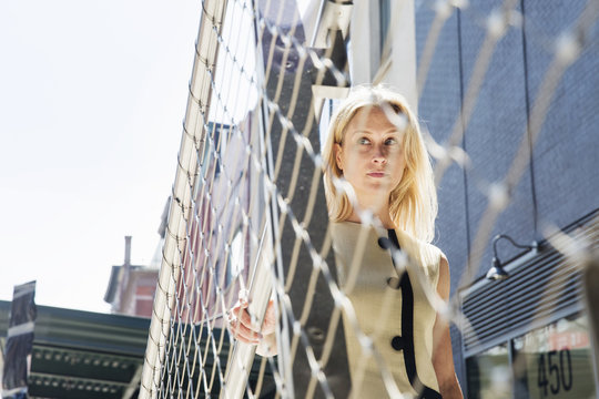 Businesswoman standing at a metal wire fence in New York.