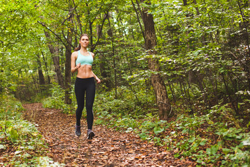 Attractive woman athlete running on path in green summer forest