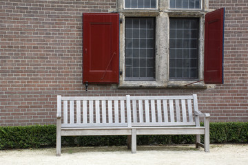 Fototapeta na wymiar Street wooden bench near the brick wall with window and red shutters