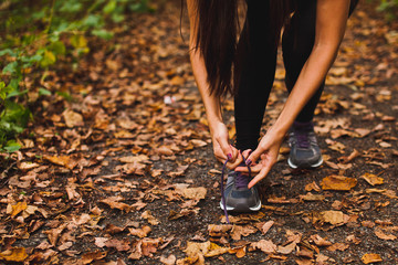Woman athlete runner tying laces at training on forest path