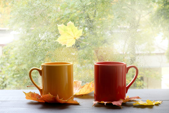 autumn warming atmosphere of comfort/ two cups on a table with leaves against the window with rain drops 