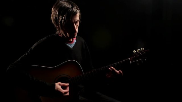 man playing guitar in dark room.