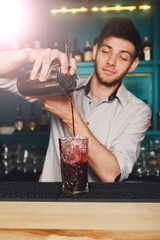Young handsome barman pouring cocktail drink into glass
