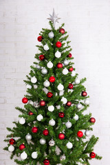 Fototapeta na wymiar Decorated christmas tree with colorful balls over white brick wa