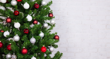 decorated christmas tree with colorful balls over white brick wa