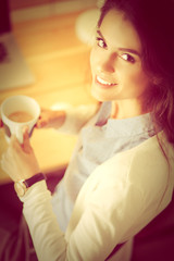 Portrait of relaxed young woman sitting at her desk holding cup of coffee