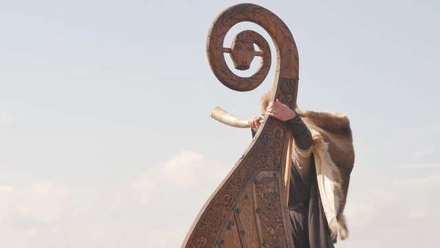 Mad viking with horn on the Drakkar on the river shore