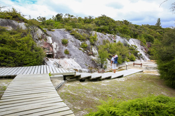 Fototapeta premium Young active father with little daughter in a back carrier standing on wooden walkboard and observing Thermal area Orakei Korako in New Zealand