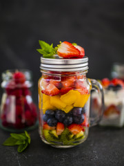 Fototapeta na wymiar Fruit salad and fresh berries fruit in a glass jars on stone background.