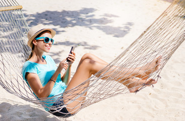 Vacation concept. Enjoying the summer. Young pretty woman in hat and sunglasses using smartphone...