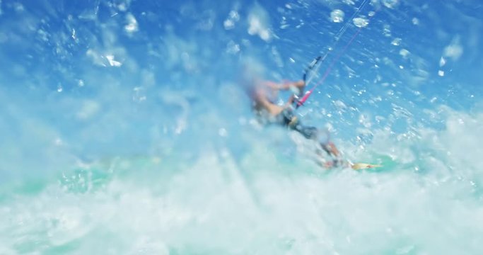 Young man kitesurfing in tropical blue ocean, splashing the camera in slow motion