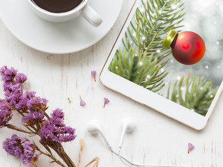 Christmas and Happy New Year 2017 concept, Black coffee and purple flowers with photo of bauble ball hanging on fir tree over abstract bokeh in tablet on white rustic wooden background